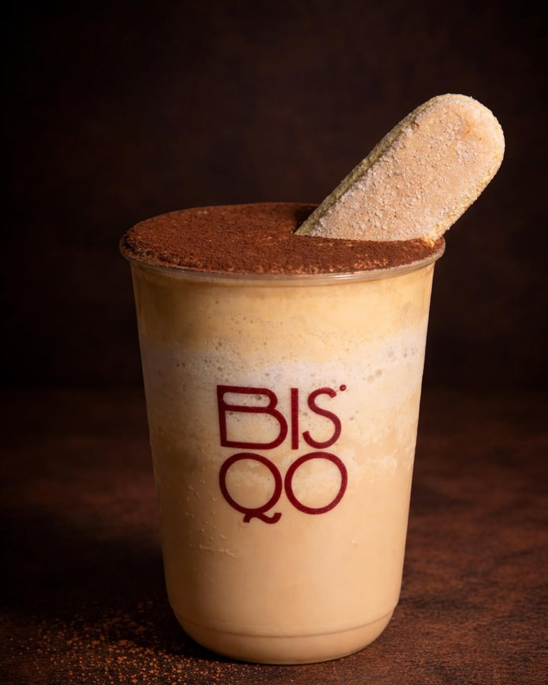 A blended tiramisu frappe in a tall cup, topped with cream and a cocoa dusting.