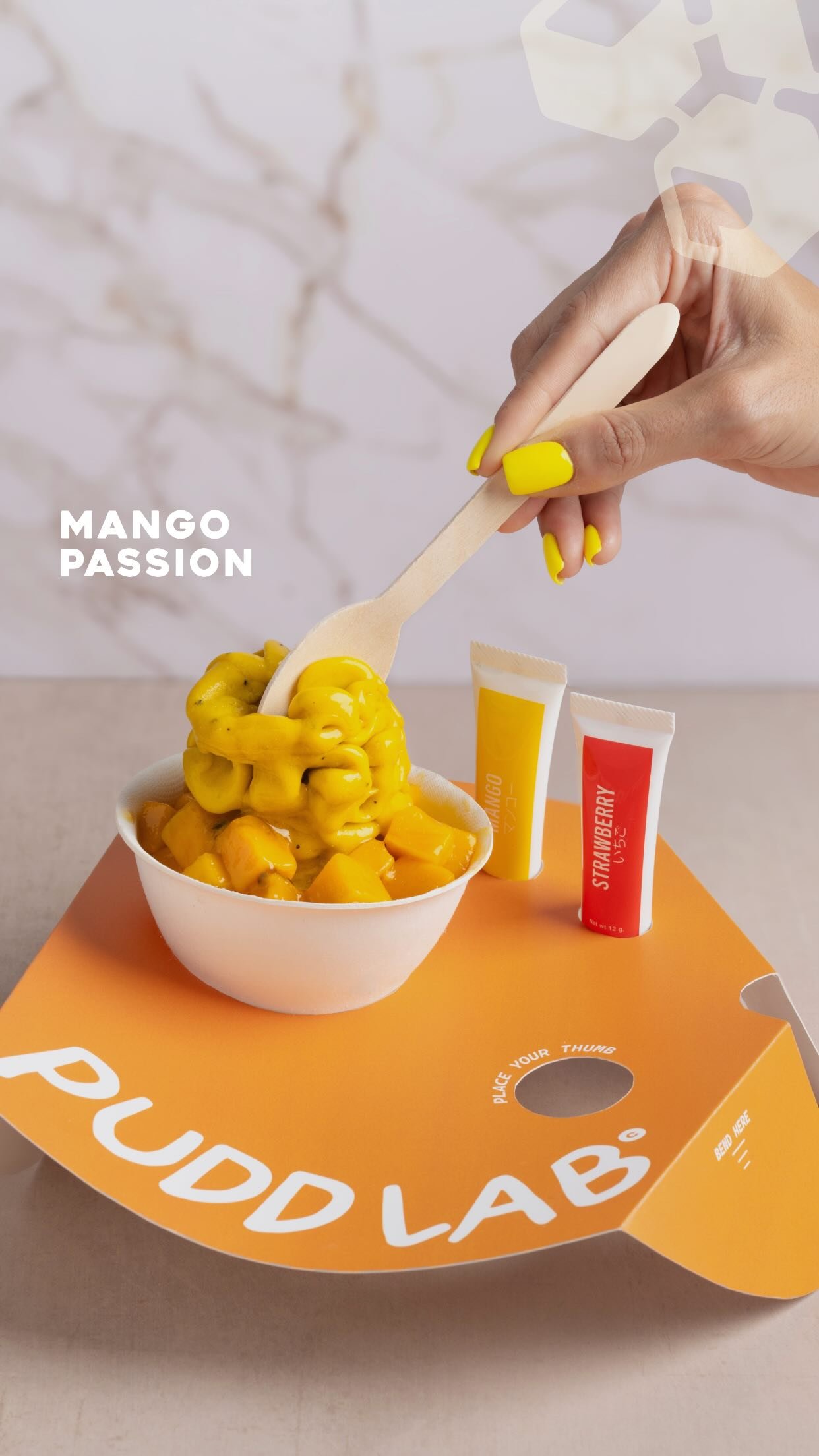 A white bowl of mango and passionfruit soft serve on a Pudd Lab tray, with branded sauce tubes beside it.
