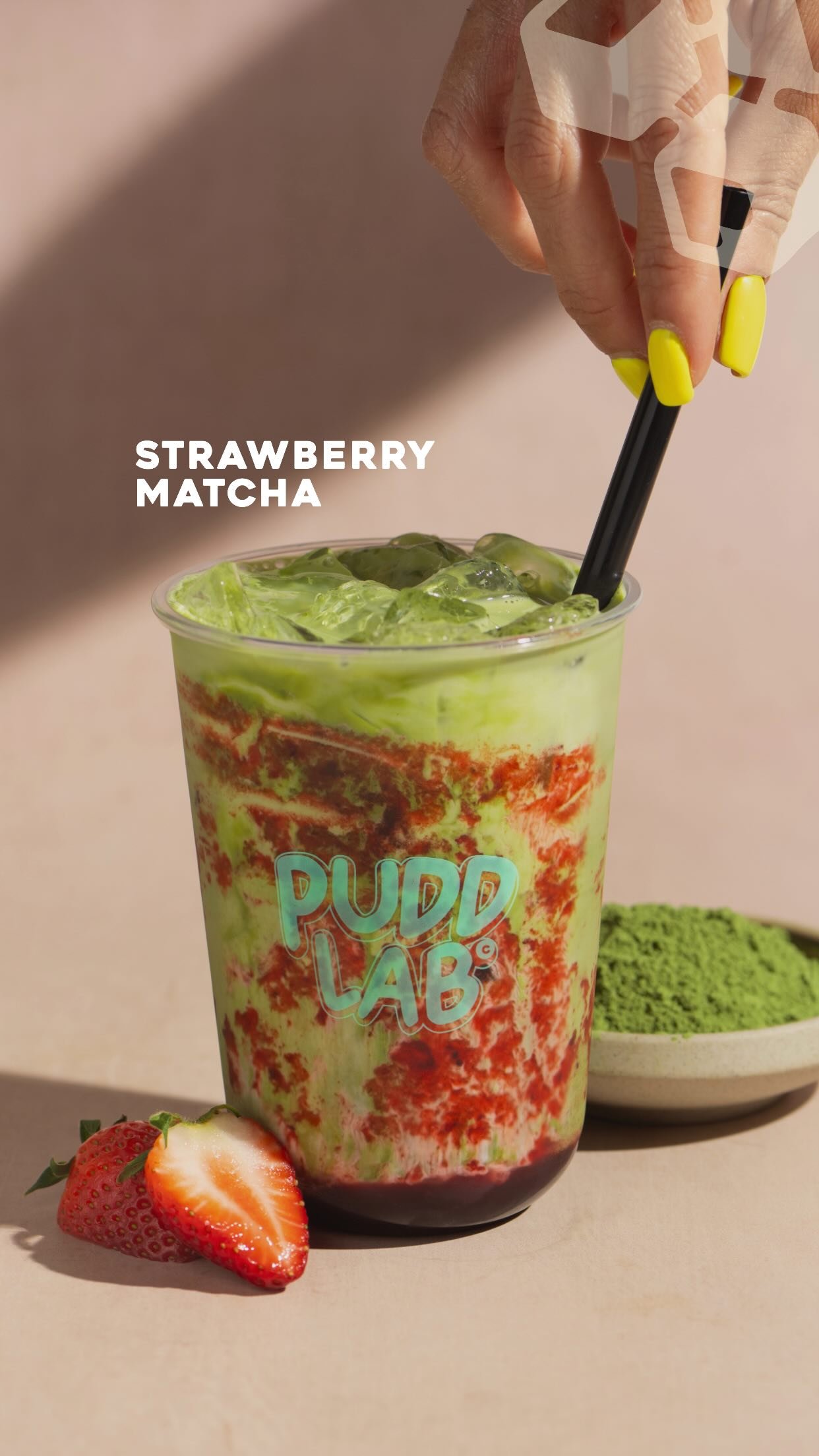 A white bowl of layered strawberry and matcha soft serve on a Pudd Lab tray, with branded sauce tubes beside it.