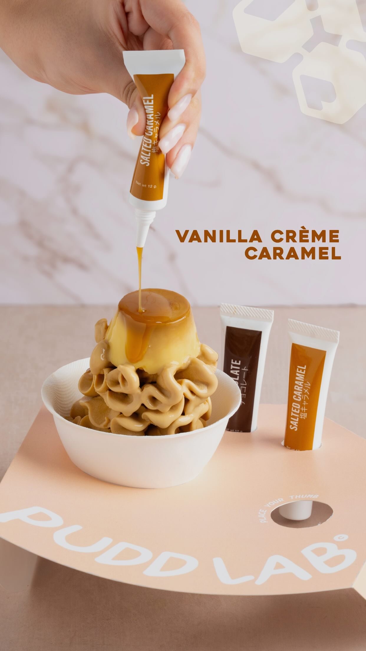 A white bowl of caramel soft serve topped with a whole crème caramel, salted caramel sauce being piped over it from a branded tube.
