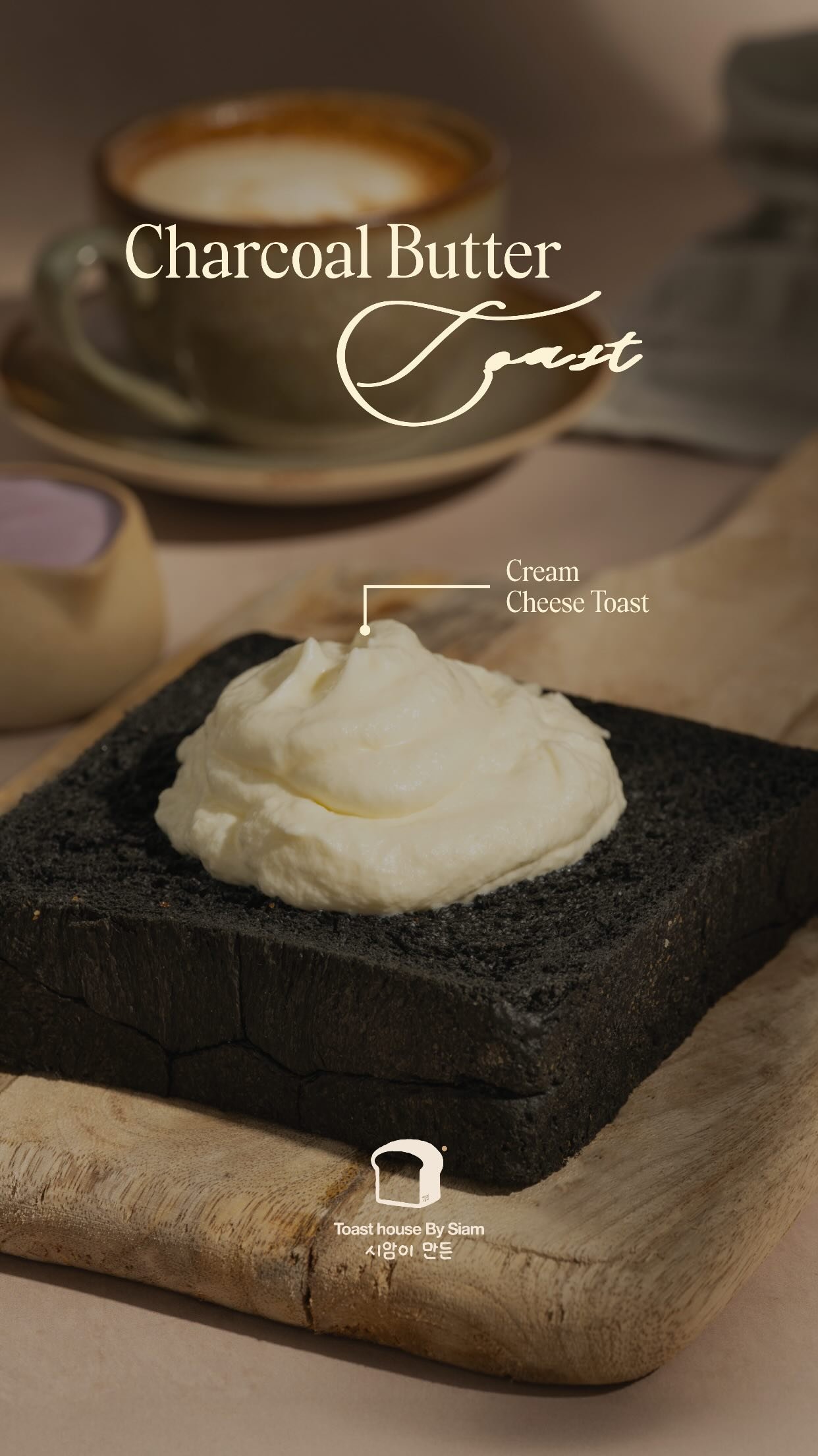 A slab of charcoal-black brioche topped with a thick swirl of cream cheese, on a wooden board beside a ceramic cup of coffee.